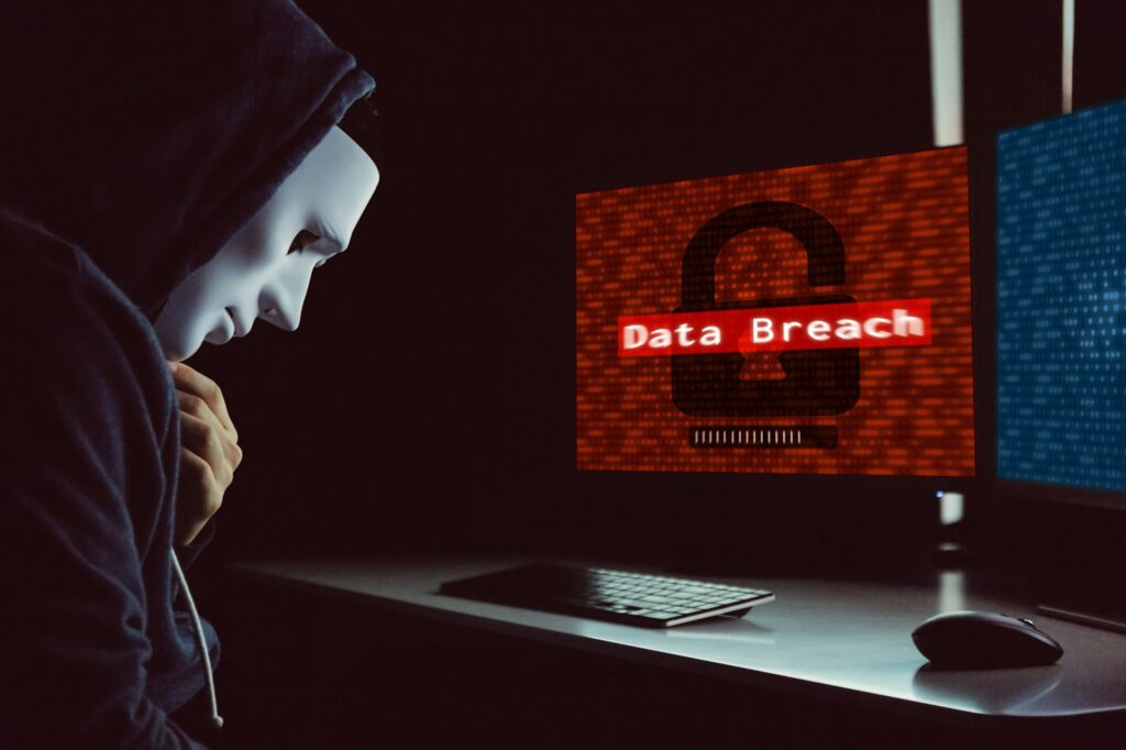 Masked hacker under hood using computer to commit data breach crime